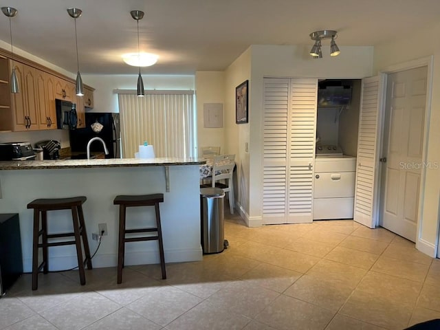 kitchen featuring washer / dryer, kitchen peninsula, hanging light fixtures, black appliances, and a breakfast bar