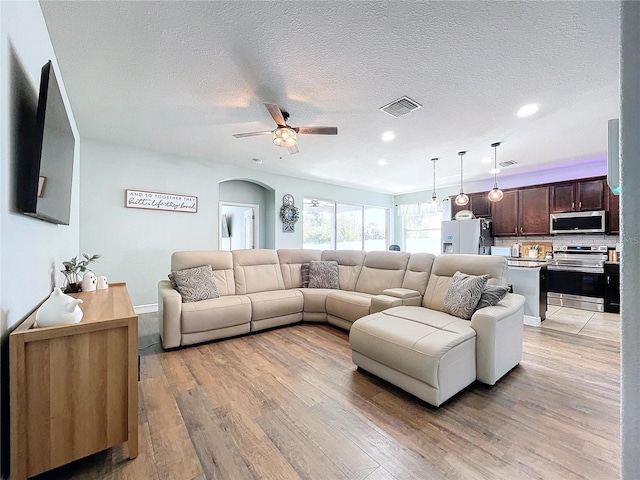 living room featuring ceiling fan, a textured ceiling, and light wood-type flooring