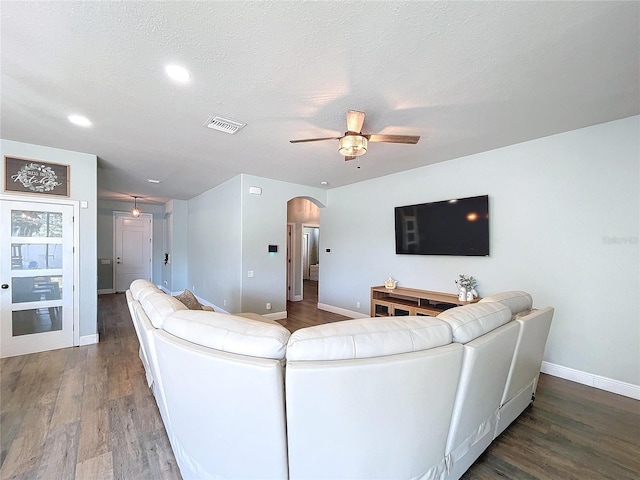 living room featuring dark wood-type flooring, a textured ceiling, and ceiling fan