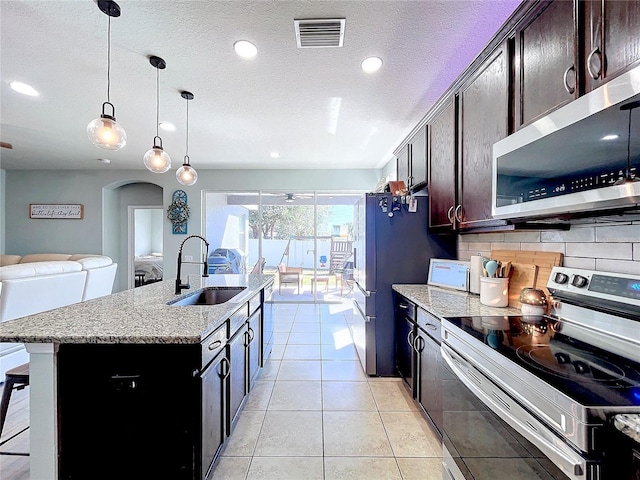 kitchen featuring decorative backsplash, a kitchen island with sink, stainless steel appliances, sink, and decorative light fixtures