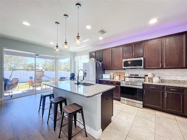 kitchen featuring light stone countertops, sink, appliances with stainless steel finishes, and a kitchen island with sink