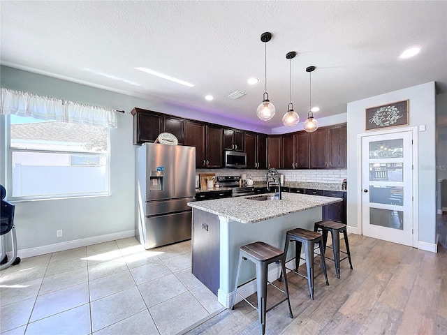 kitchen with decorative backsplash, an island with sink, stainless steel appliances, sink, and light hardwood / wood-style floors