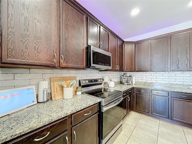 kitchen featuring decorative backsplash, stainless steel appliances, light stone countertops, light tile patterned flooring, and dark brown cabinetry