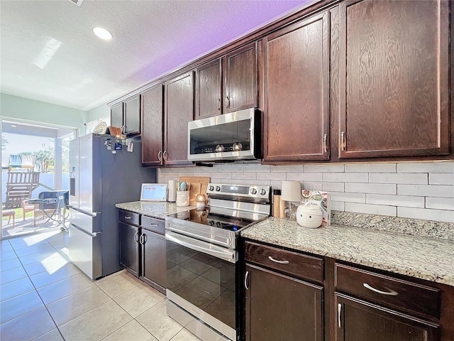 kitchen with tasteful backsplash, light stone counters, light tile patterned floors, dark brown cabinetry, and stainless steel appliances