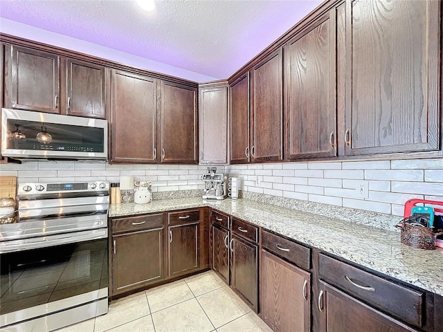 kitchen with light stone counters, backsplash, light tile patterned floors, a textured ceiling, and stainless steel appliances