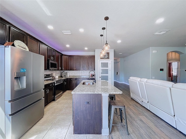 kitchen with tasteful backsplash, a center island with sink, appliances with stainless steel finishes, dark brown cabinetry, and sink