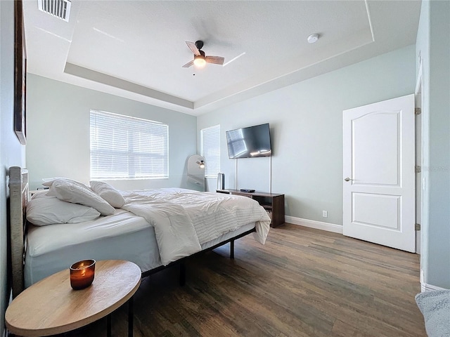 bedroom with dark hardwood / wood-style floors, a tray ceiling, and ceiling fan