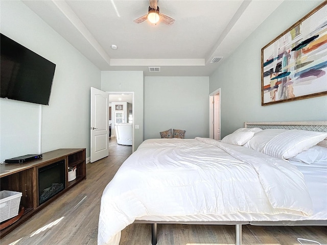 bedroom with ceiling fan, a raised ceiling, and wood-type flooring