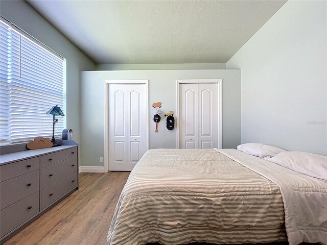 bedroom with multiple closets, a textured ceiling, and light wood-type flooring