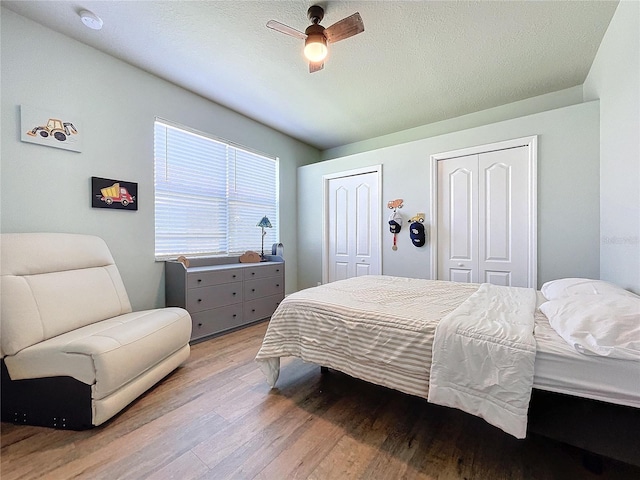 bedroom with ceiling fan, multiple closets, a textured ceiling, and light wood-type flooring