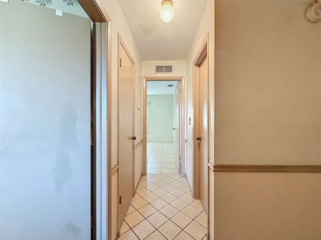 hall with a textured ceiling and light tile patterned floors