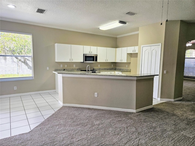 kitchen with a wealth of natural light, white cabinetry, light colored carpet, and a textured ceiling