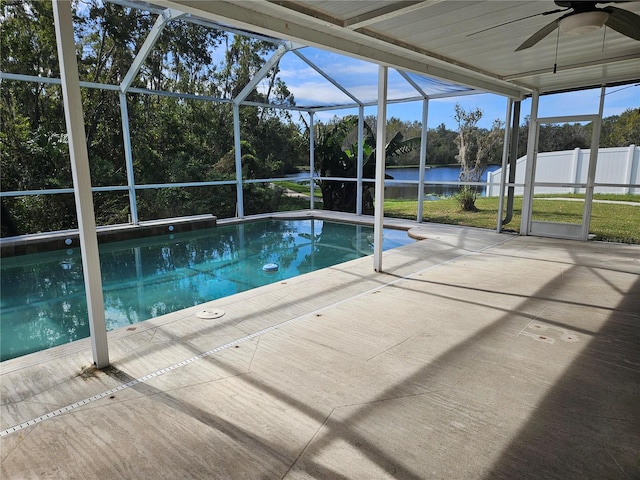 view of swimming pool with glass enclosure, ceiling fan, a water view, and a patio area