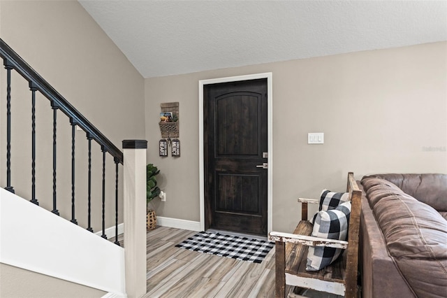 entrance foyer featuring lofted ceiling, a textured ceiling, and light wood-type flooring