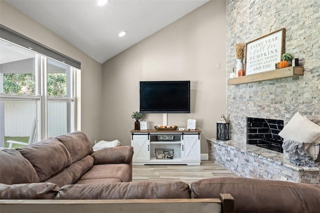 living room featuring light hardwood / wood-style flooring, lofted ceiling, and a stone fireplace