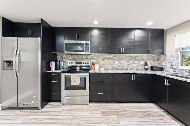 kitchen featuring light stone countertops, appliances with stainless steel finishes, light hardwood / wood-style flooring, and backsplash