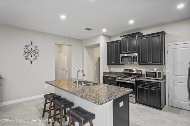 kitchen with sink, stainless steel appliances, dark stone counters, a breakfast bar area, and a kitchen island with sink