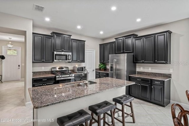 kitchen with a breakfast bar, stainless steel appliances, a kitchen island with sink, sink, and light tile patterned flooring