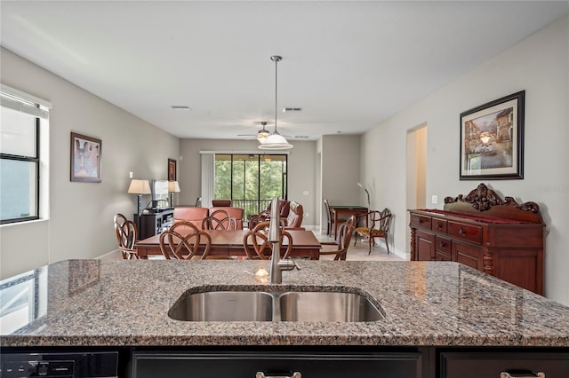 kitchen featuring sink, ceiling fan, an island with sink, decorative light fixtures, and light stone counters