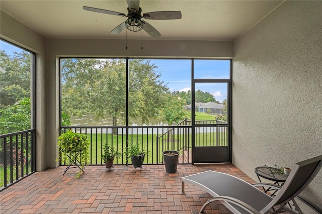 sunroom with ceiling fan and a water view