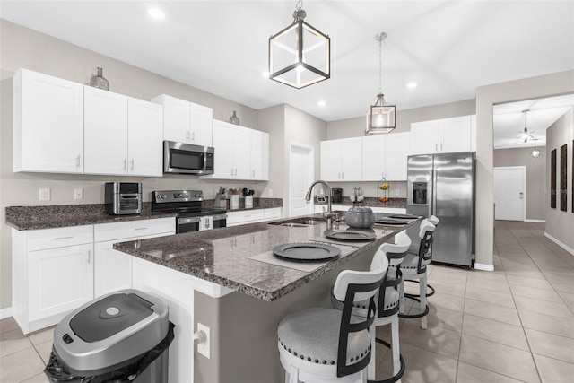 kitchen with appliances with stainless steel finishes, sink, an island with sink, white cabinetry, and decorative light fixtures