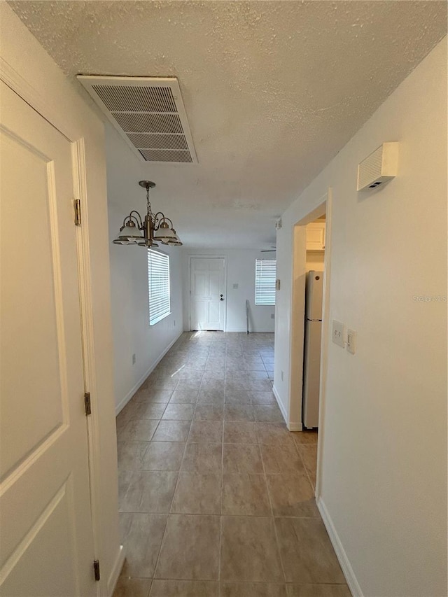 hallway with a textured ceiling, an inviting chandelier, a healthy amount of sunlight, and light tile patterned flooring