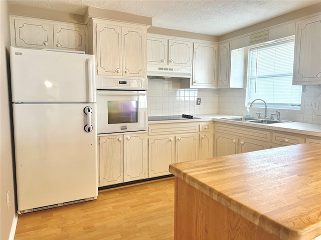 kitchen with sink, white appliances, decorative backsplash, and light wood-type flooring