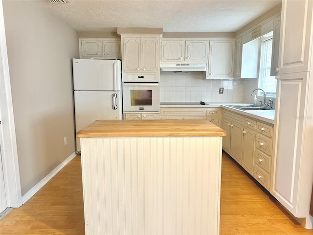 kitchen featuring a kitchen island, sink, backsplash, white appliances, and light hardwood / wood-style flooring