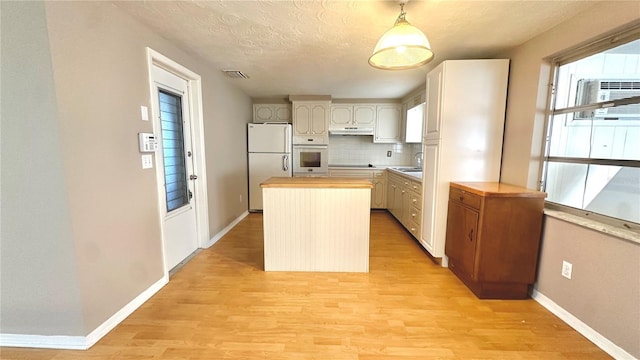 kitchen with white appliances, backsplash, hanging light fixtures, light hardwood / wood-style floors, and a kitchen island