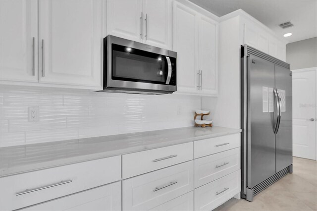 kitchen with light stone counters, stainless steel appliances, decorative backsplash, and white cabinets