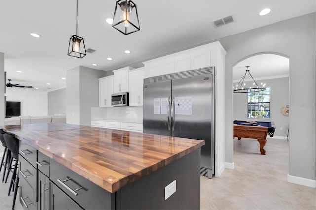 kitchen with white cabinetry, wood counters, stainless steel appliances, decorative light fixtures, and a center island