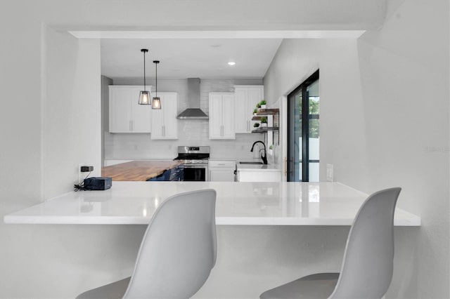 kitchen featuring white cabinetry, wall chimney range hood, decorative light fixtures, and stainless steel stove