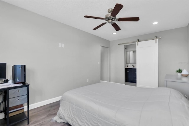 bedroom with ceiling fan, a barn door, hardwood / wood-style flooring, connected bathroom, and sink