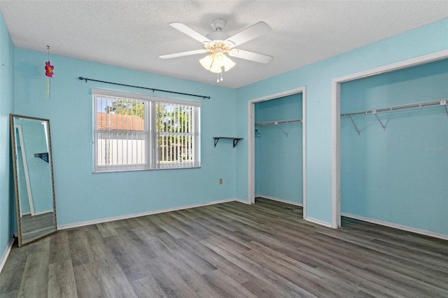 unfurnished bedroom with dark wood-type flooring, ceiling fan, a textured ceiling, and two closets