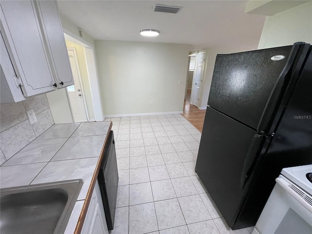 kitchen featuring tile countertops, sink, black appliances, and white cabinets