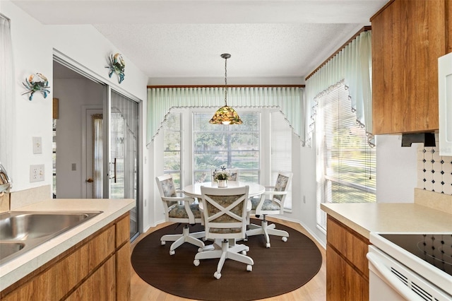 kitchen featuring a textured ceiling, stove, light wood-type flooring, sink, and decorative light fixtures