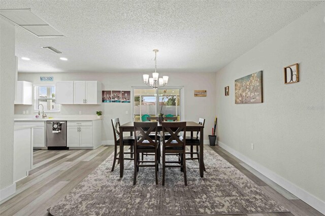 dining area featuring a textured ceiling, a healthy amount of sunlight, a chandelier, and light wood-type flooring