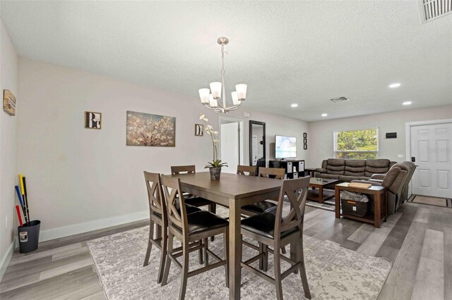 dining area with light hardwood / wood-style flooring, a textured ceiling, and an inviting chandelier