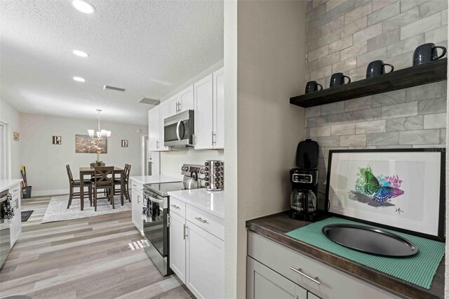 kitchen with tasteful backsplash, appliances with stainless steel finishes, hanging light fixtures, light hardwood / wood-style floors, and white cabinets