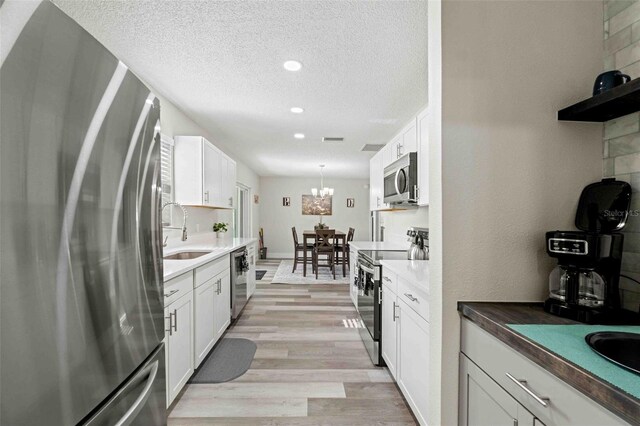 kitchen featuring appliances with stainless steel finishes, sink, light wood-type flooring, white cabinetry, and decorative light fixtures