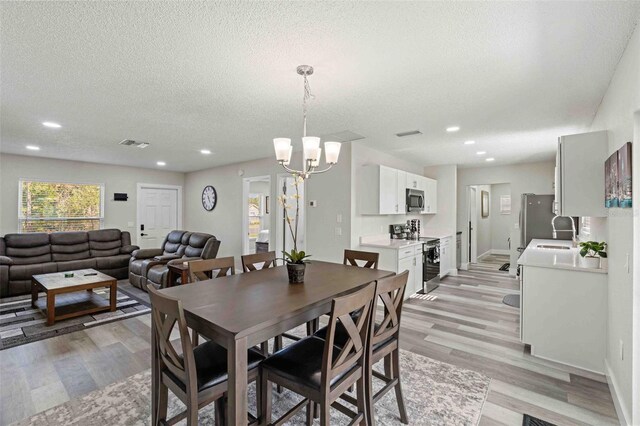 dining room featuring an inviting chandelier, a textured ceiling, sink, and light wood-type flooring