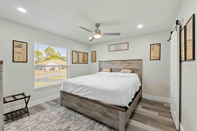 bedroom featuring a textured ceiling, a barn door, wood-type flooring, and ceiling fan