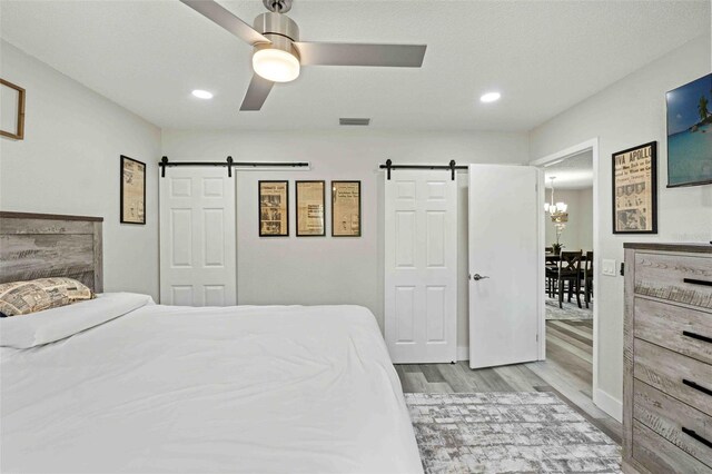 bedroom with ceiling fan with notable chandelier, light hardwood / wood-style floors, and a barn door