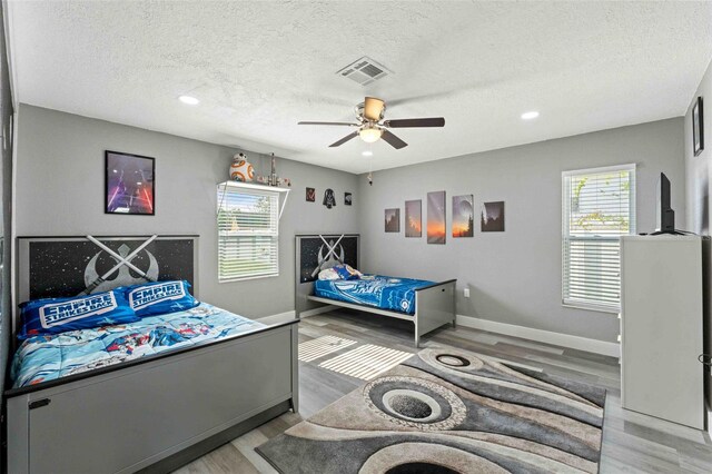 bedroom with light hardwood / wood-style flooring, a textured ceiling, and ceiling fan