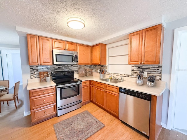 kitchen with decorative backsplash, appliances with stainless steel finishes, sink, and light hardwood / wood-style floors