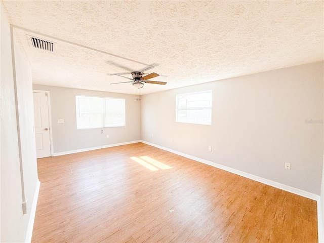 spare room with a textured ceiling, light wood-type flooring, and a healthy amount of sunlight