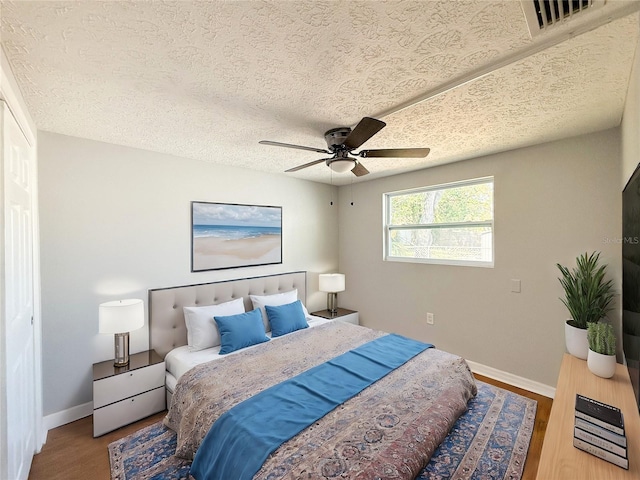 bedroom with hardwood / wood-style floors, ceiling fan, and a textured ceiling