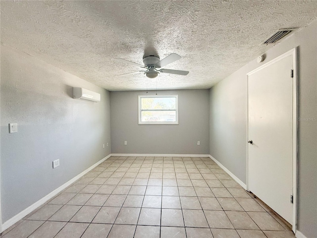 unfurnished room with a textured ceiling, a wall unit AC, ceiling fan, and light tile patterned floors