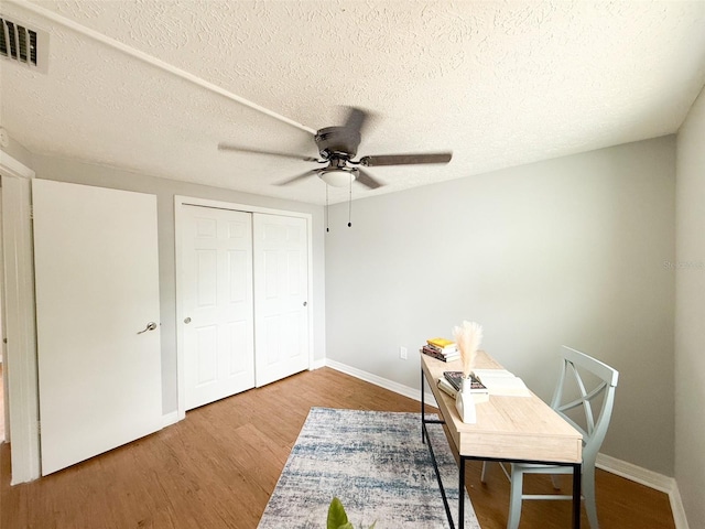 home office featuring a ceiling fan, wood finished floors, baseboards, and a textured ceiling