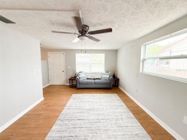 living area featuring ceiling fan, light wood-style floors, baseboards, and a textured ceiling